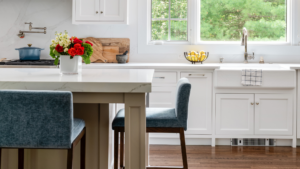 Bright custom kitchen showcasing thoughtful home renovation planning with white cabinetry, quartz countertops, farmhouse sink, blue seating, and coordinated finishes.
